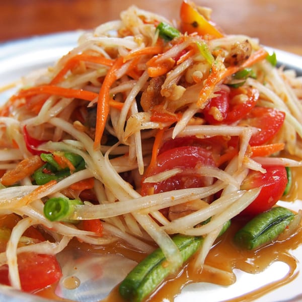 Close-up of a vibrant Thai papaya salad with shredded papaya, carrots, tomatoes, and green beans.