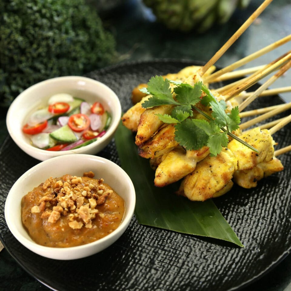 Laem Buri's chicken satay skewers with peanut sauce and cucumber relish on a black plate.